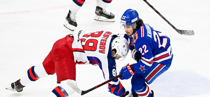 Хоккеисты в красной и синей форме противостоят друг другу на льду. Игрок в синей форме ведет шайбу, игрок в красной форме пытается атаковать соперника. На форме видны номера 89 и 22